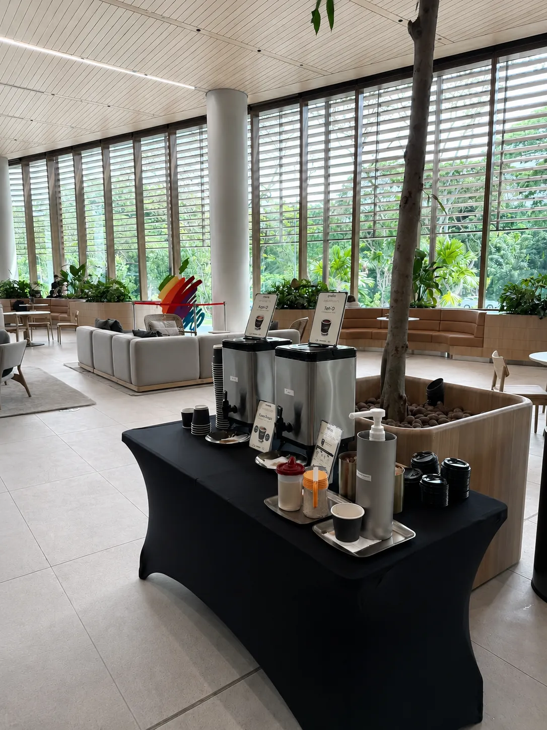 A Genista Ln pre-brew station with labelled Kopi O and Teh O urns on a black skirted table in a bright corporate office lobby in Singapore.