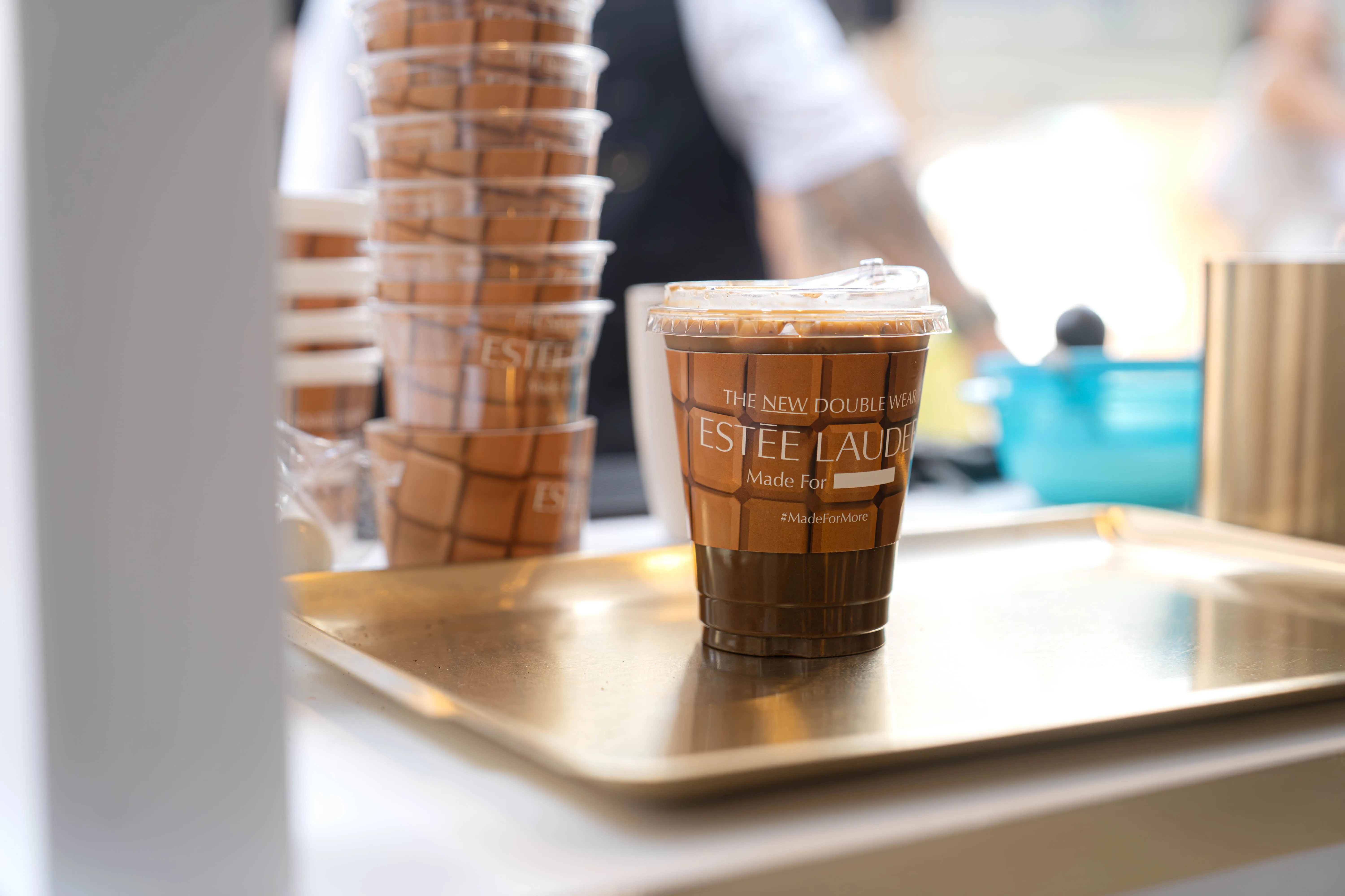 An iced kopi in a cup custom-printed for the Estée Lauder Double Wear launch, with a stack of matching printed cups behind it.