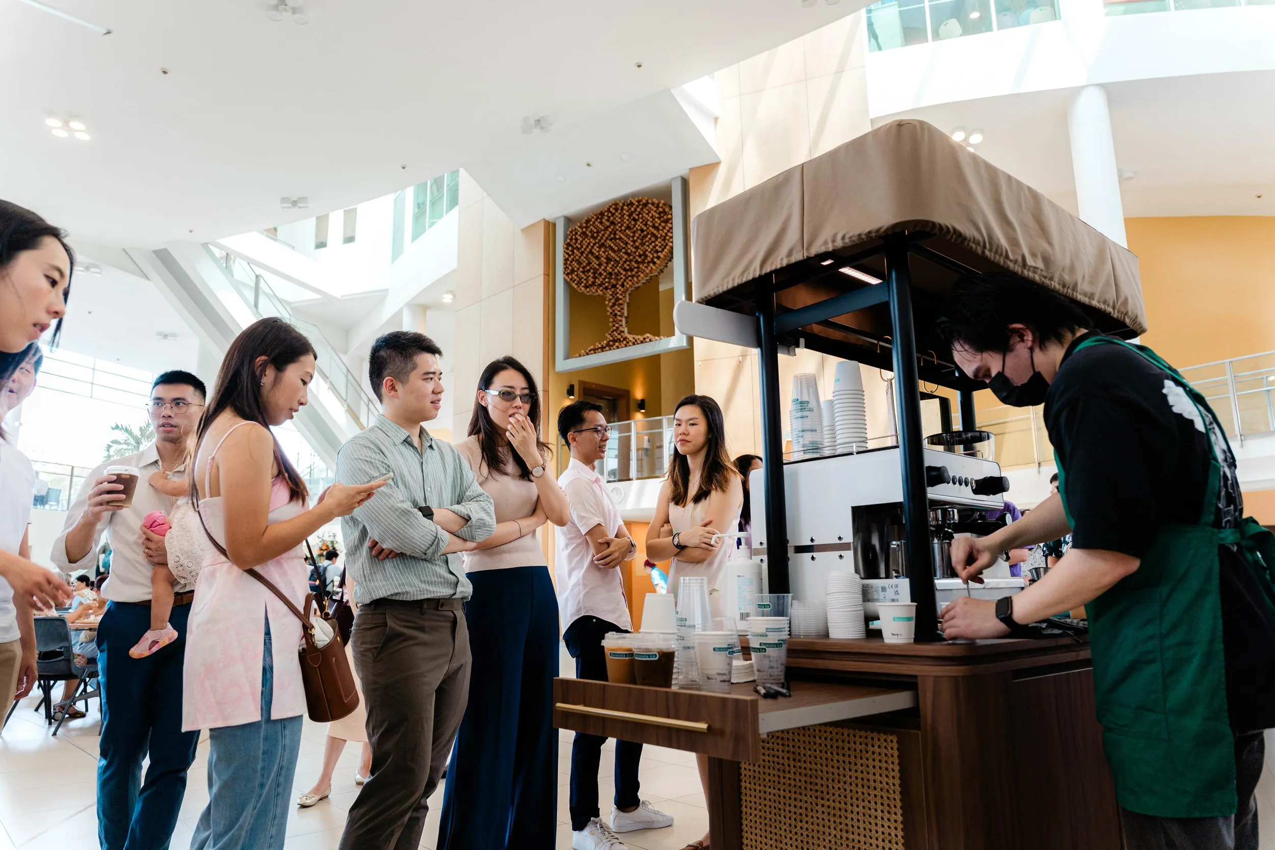Wedding guests wait for drinks as a barista prepares kopi at the cart in a bright church hall