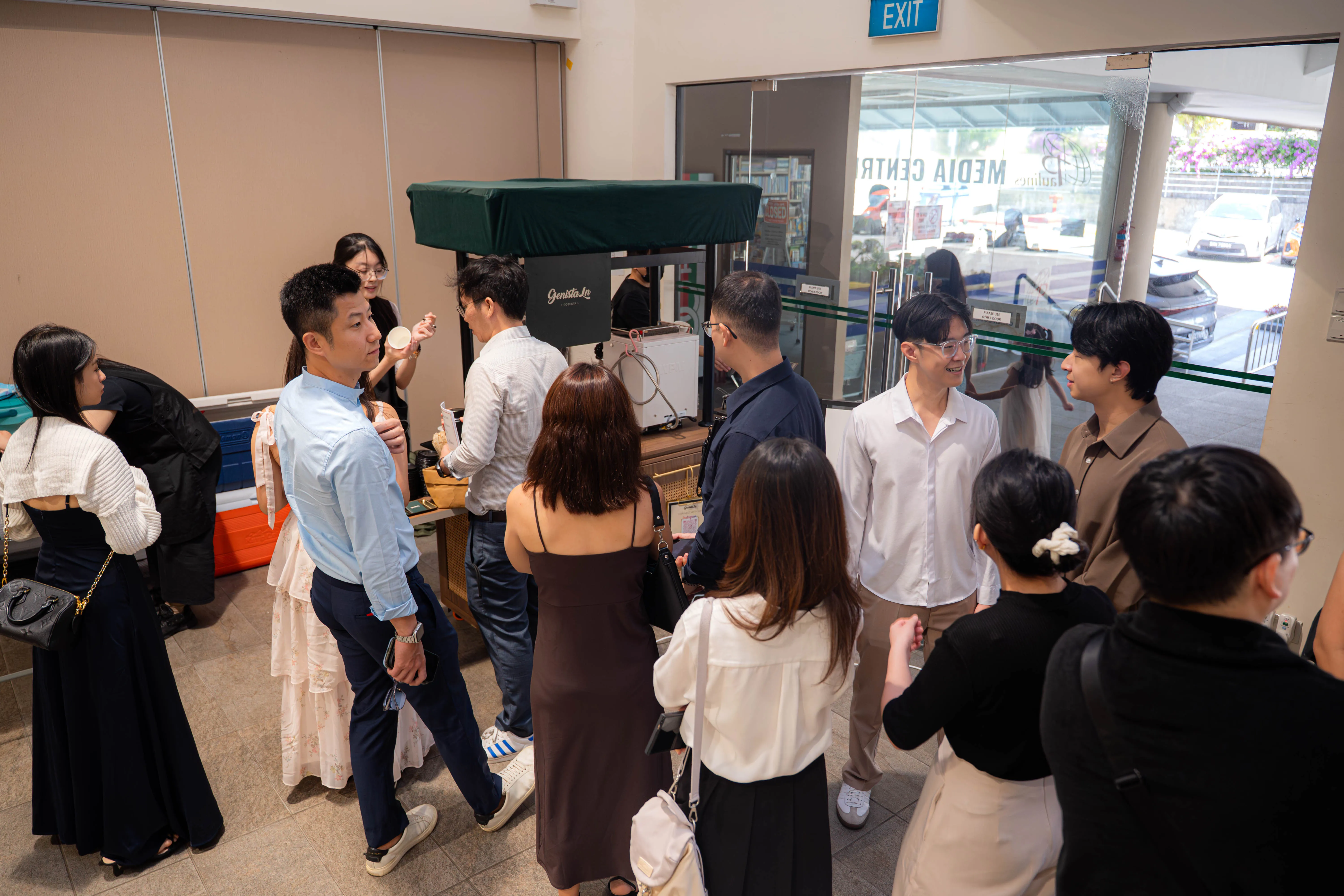 Wedding guests gathered around the Genista Ln cart in a church foyer, several already holding cups and talking in groups.
