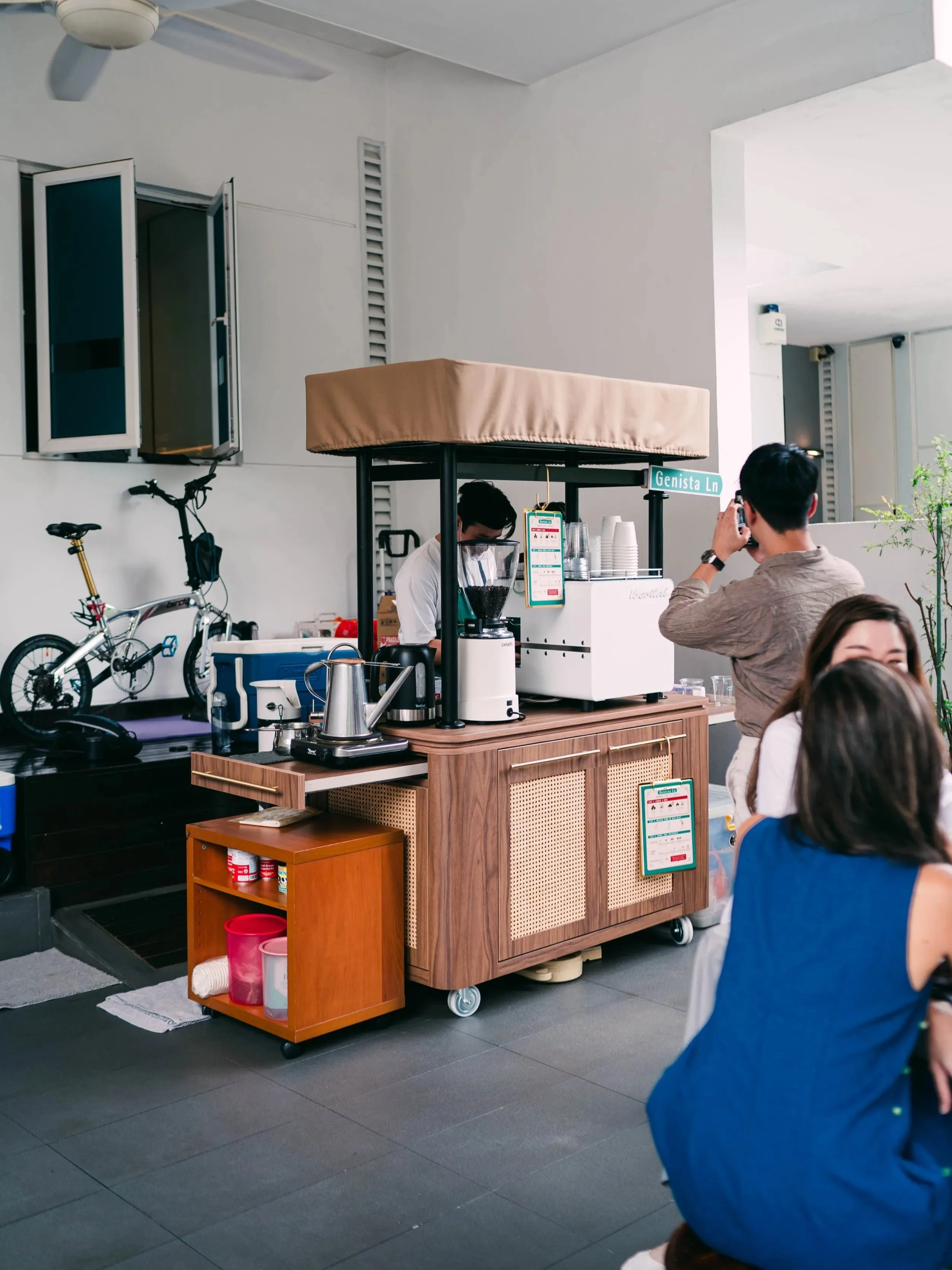 The Genista Ln kopi cart set up in the open car porch of a landed house, a barista working behind it while guests gather to order.
